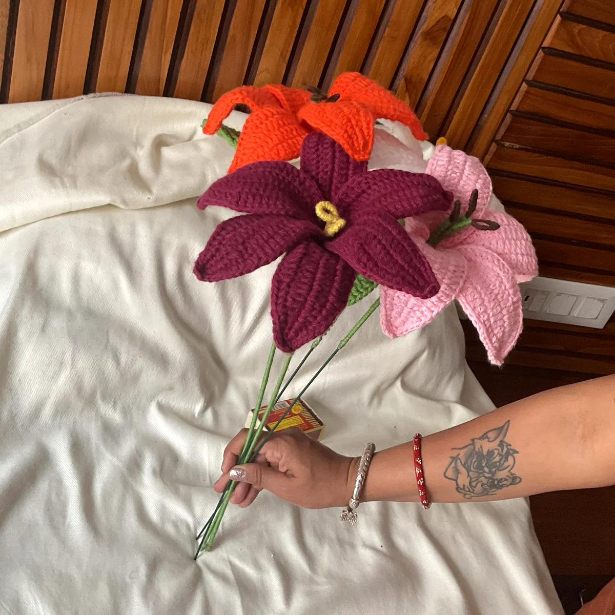 A maker's hand holding a bouquet of crochet lilies